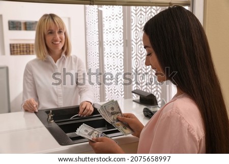 Young woman with money at cash department window in bank. Currency exchange Royalty-Free Stock Photo #2075658997
