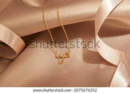 golden ribbon pendant with gold chain isolated on silk background