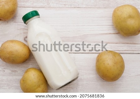 Potato milk in a glass bottle on a white wooden background. New, young potatoes are on the table. Healthy vegetarian non-dairy drink, Alternative milk, copy space, top view.
