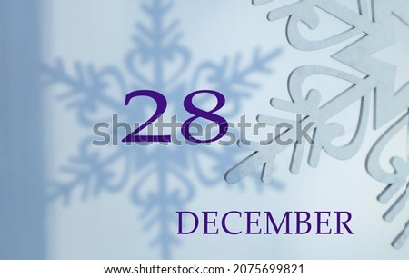 Calendar for December 28: name of the month in English, number 28 on a blue background of snowflakes and their shadows.