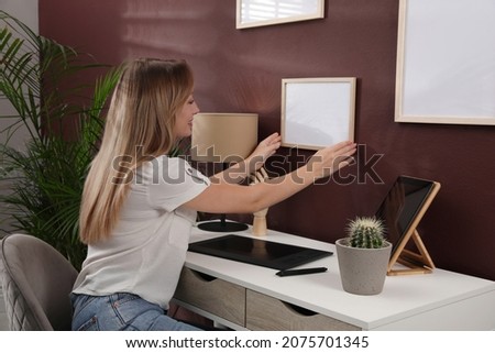 Young woman hanging empty frame on brown wall indoors. Mockup for design