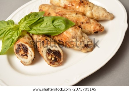 Meat roll with dried apricots, prunes and walnuts inside. Chicken Meat cannelloni stuffed with dried fruits and nuts. Served with fresh basil leaf on white vintage plate on gray solid background 