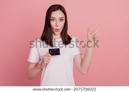 Photo of young lady amazed surprised indicate finger empty space advertising hold credit card isolated over pink color background
