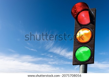 Closeup of a traffic light on a blue sky with clouds and copy space, with all three lights on, green, orange and red. Italy, Europe. Royalty-Free Stock Photo #2075708056