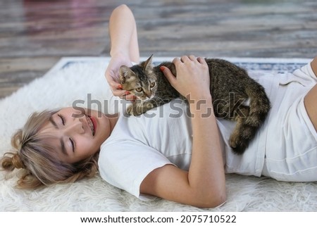 Young girl with cat on couch at home. The girl's fingers are playing with a cat lying on her chest.