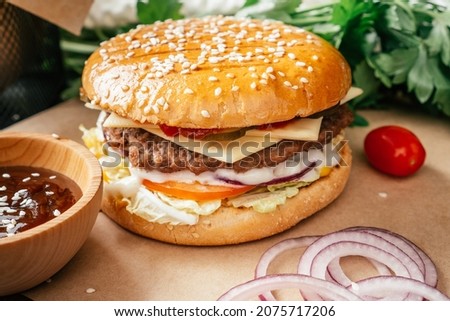 Classic double burger with meat cutlet, lettuce, tomato, pickled cucumber, cheese, onion and sauce on craft paper with cherry tomatoes and green parsley