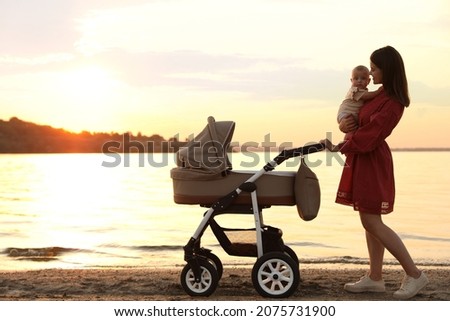 Happy mother with baby walking near river at sunset