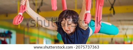 Senior mature woman practices anti-gravity yoga with a hammock in a studio. Lifestyle BANNER, LONG FORMAT