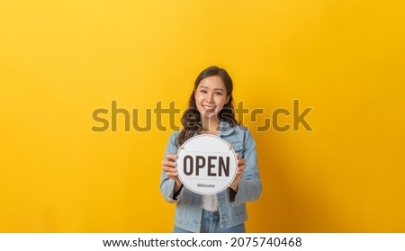 Reopening. attractive asian female in denim Jacket clothing smiling holding open sign board with copy space for text on yellow background, advertising, online marketing, reopen announcement concept