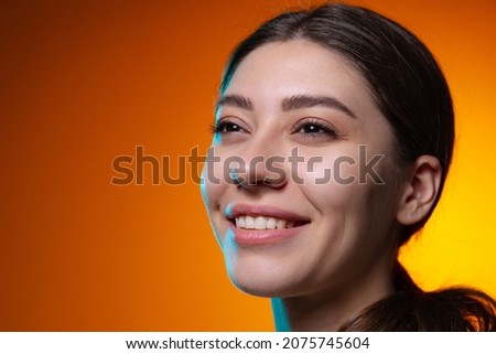 Charming smile. Close-up portrait of young beautiful smiling girl isolated on yellow brown studio background in neon light. Concept of emotions, facial expression, youth, aspiration. Copy space for ad