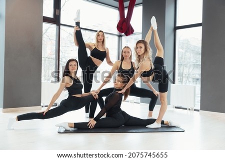 Grace, flexibility and beauty. Young slim fit girls in black sportswear posing at yoga position at sport center, indoors. Concept of healthy lifestyle, sport, wellness, wellbeing, mental health.