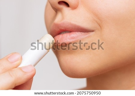 Cropped shot of a young caucasian beautiful woman applying a hygienic lipstick on her lips on a gray background. Moisturizing chapstick for dry lips Royalty-Free Stock Photo #2075750950