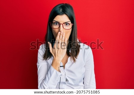 Young hispanic woman using lavalier microphone covering mouth with hand, shocked and afraid for mistake. surprised expression 