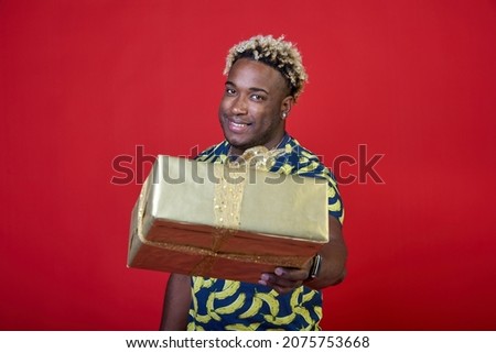Smiling young African-American gives a gift in a gold package on a red background. Black man makes a surprise