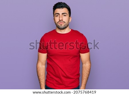 Hispanic man with beard wearing casual red t shirt relaxed with serious expression on face. simple and natural looking at the camera. 