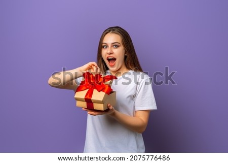 Emotional brunette young woman opening box with birthday gift, having overjoyed ecstatic facial expression, keeping her mouth wide opened, feeling grateful for such a surprise