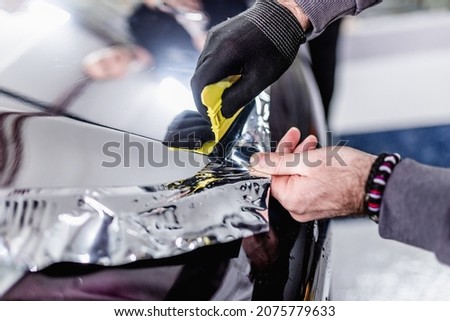 Car wrapping specialist putting silver mirror chrome foil on car. Selective focus.  Royalty-Free Stock Photo #2075779633