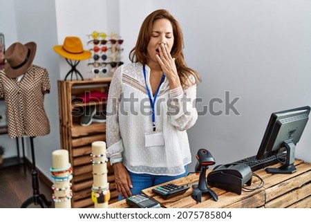 Middle age hispanic woman working as manager at retail boutique bored yawning tired covering mouth with hand. restless and sleepiness. 