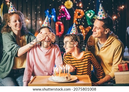 Happy parents and children trying to blow burning candles on delicious birthday cake celebrate holiday in cottage yard in evening