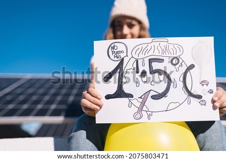 Teenage girl protests next to solar panels with a painted sign calling for preventing the earth's temperature from rising by 1.5 degrees Celsius. Awareness of the new generations. Climate summit