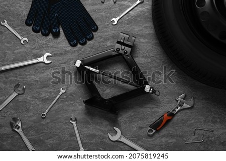 Car wheel, scissor jack, gloves and different tools on grey stone surface, flat lay