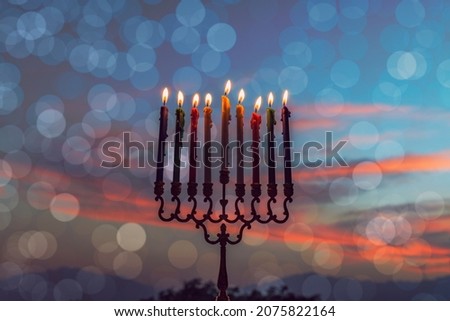 Burning wax festive candles are traditional symbols of Hanukkah Hebrew Holiday of Light, selective focus on menorah with burning  wax candles, blurred mountains, dramatic dawn sky background, bokeh 