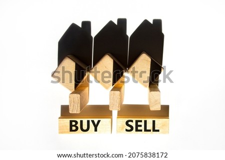 Buy or sell house symbol. Concept words 'Buy Sell' on wooden blocks near miniature houses from shadows. Beautiful white background, copy space. Business and buy or sell house concept.