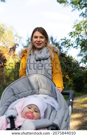 Picture of young cheerful caucasian lady walking her baby with a stroller outdoor. Baby having a pacifier