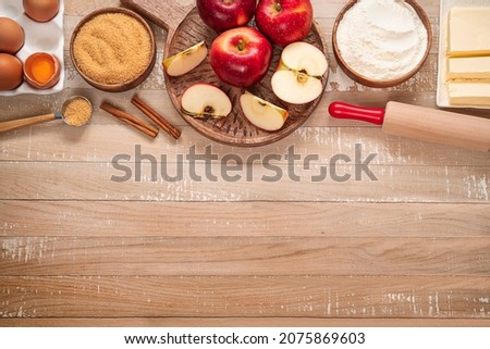 Top table view on ingredients for Apple pie or Charlotte on light wooden background. Ingredients for apple pie - red apples, flour, eggs, sugar, cinnamon and butter on a wooden table Royalty-Free Stock Photo #2075869603