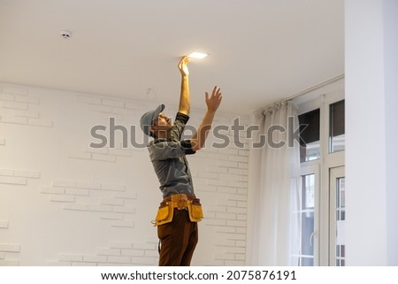 Electrician worker installation electric lamps light inside apartment. Construction decoration concept. Royalty-Free Stock Photo #2075876191