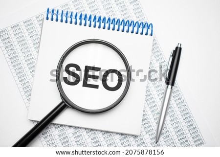 In the notebook is the text of seo, next to the black pen, magnifying glass. A business concept.