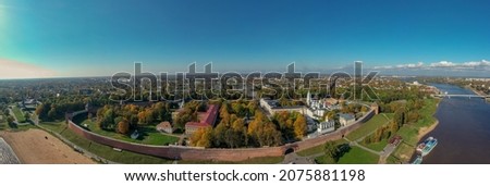 Panoramic aerial view of the Kremlin in Veliky Novgorod, golden autumn in the city, yellow treetops, a bridge over the Volkhov river, city sandy beach, a fortress
