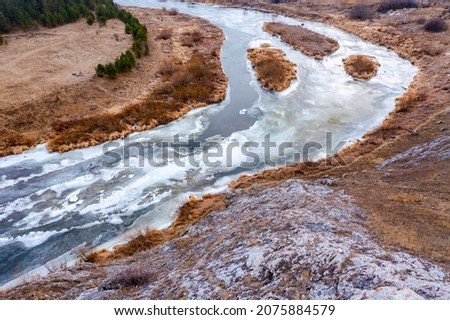 aerial top view of river bend with snowy frozen shore and bare trees in winter day