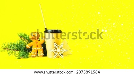 Coffee in paper cup with wooden tube and gingerbread man on trendy yellow background.Festive greeting card or Christmas decor. Creative copy space. Close-up
