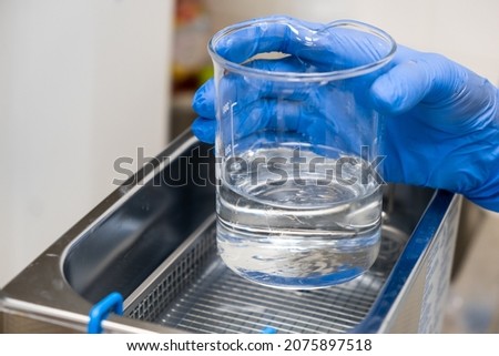 Scientist in blue rubber puts a beaker for dissolving or cleaning into an ultrasound bath. Clinical, toxicological and forensic analysis.