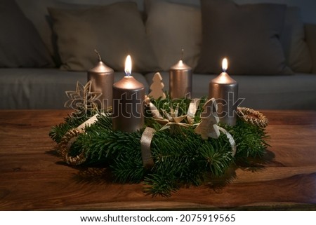 Two golden candles are lit for the second Sunday on an Advent wreath wth natural Christmas decoration on a wooden coffee table, copy space, selected focus, narrow depth of field