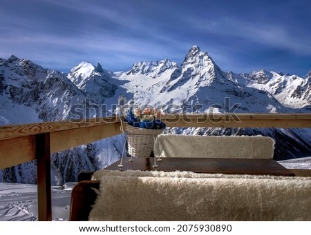 Flowers in a vase on a wooden table on the balcony overlooking the mountains of the Caucasus Range on a sunny day in winter
