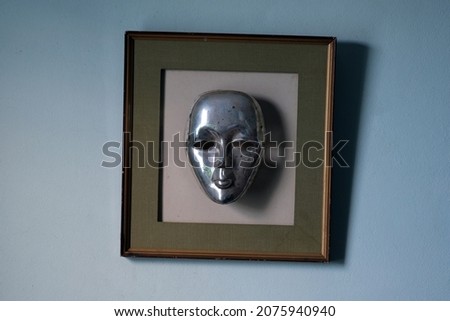 A dirty silver mask on an old picture frame adorns the building's walls.