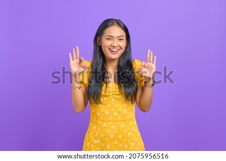 Cheerful young Asian woman makes okay gesture, demonstrates symbol of approval on purple background
