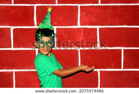 Latin child happy and excited for the arrival of December and celebrating Christmas shows his enthusiasm with hat and green Christmas glasses
