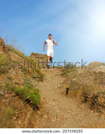 Young man in fitness clothing running along mountain with the blue sky in the background and open space around him