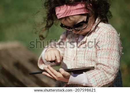 curly little girl uses tablet outdoors