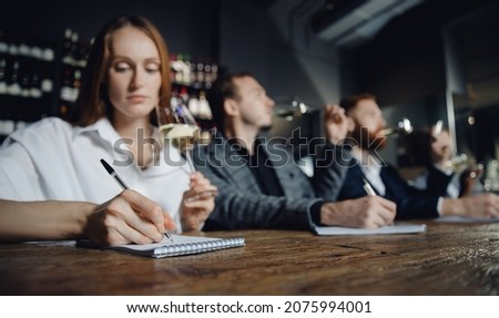 Sommeliers female and male tasting white wine and making notes at degustation card notepad. Royalty-Free Stock Photo #2075994001