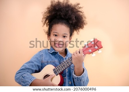 Happy little smiling african american girl playing ukulele in living room. isolated on Yellow.