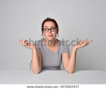 close up portrait of girl sitting at a table with natural hand gestures, wearing striped shirt and hair in bun. isolated on studio background.