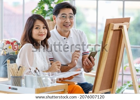 Senior man and woman couple, husband and wife, painting image together in home gallery with warm and happy circumstance. Idea for time-sharing and relaxing for older people after retirement.
