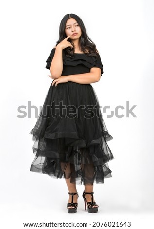 Full-body portrait shot a cute smiling young girl teenager in beautiful black dress raising hand up and looking at camera in studio isolated white background. Junior girl dancing with happiness