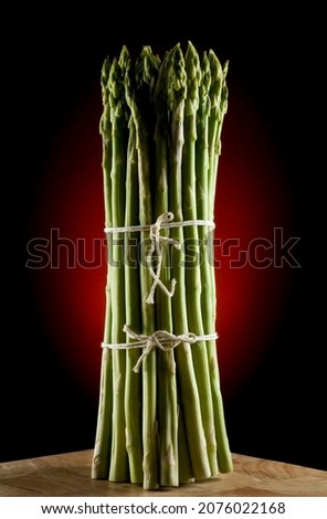 Bunch of asparagus spears on timber bench with red spot on background