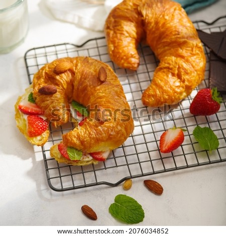 A beautiful composition - two croissants with strawberries, mint leaves and almond nuts, pieces of chocolate on a white background. Sweet food, delicious nutritious vitamin breakfast.
