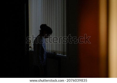 trouble and problem concept of domestic violence upset sad little girl on blue window background in sunset home room Royalty-Free Stock Photo #2076039835